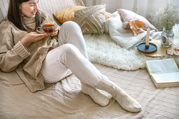 Gemütlicher Herbst zu Hause, eine Frau in einem Strickpullover mit einer Tasse Tee.