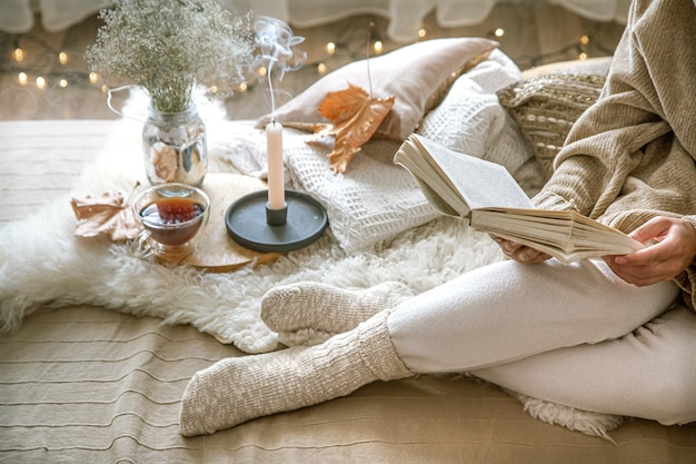 Gemütlicher herbst zu hause, eine frau mit einem buch, das sich ausruht. eine gemütliche lebensweise. körperteile in der zusammensetzung.
