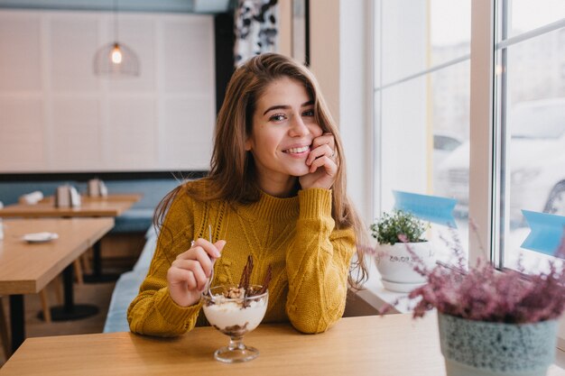 Gemütliches Porträt der schönen jungen Frau, die in der Winterzeit im bequemen Café kühlt. Fröhliche Stimmung, positive Gefühle, langes brünettes Haar. Lecker, Dessert, süßes Leben.