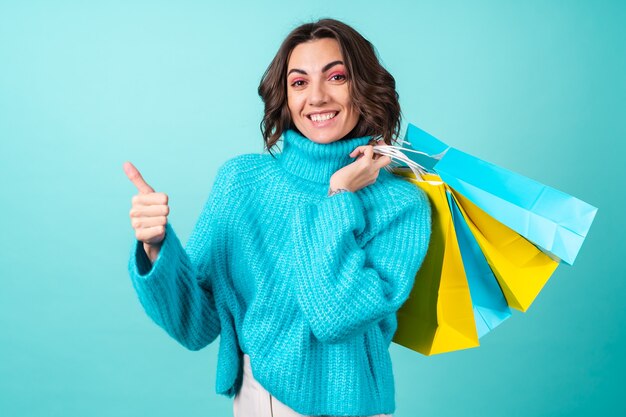 Gemütliches Porträt einer jungen Frau in einem gestrickten blauen Pullover und leuchtend rosa Make-up auf Türkis mit Einkaufstüten