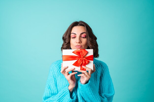 Gemütliches Porträt einer jungen Frau in einem gestrickten blauen Pullover und leuchtend rosa Make-up mit einer Geschenkbox