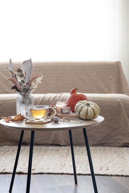 Gemütliches Wohnstilleben mit einer Tasse Tee, Kürbissen, Kerzen und Herbstdekordetails auf einem Tisch auf einem unscharfen Hintergrund des Raumes.