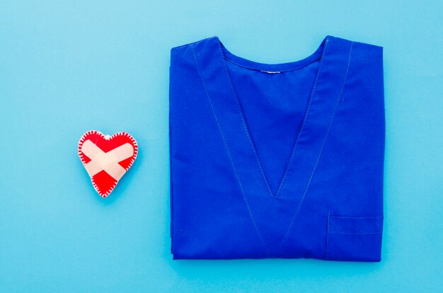 Genähtes Herz mit selbstklebendem Verband nahe dem medizinischen Kleid auf blauem Hintergrund