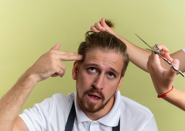 Genervt von einem jungen, gutaussehenden Friseur, der Selbstmord gestikuliert und mit jemandem aufschaut, der hält und sich bereit macht, seine auf Olivgrün isolierten Haare zu schneiden