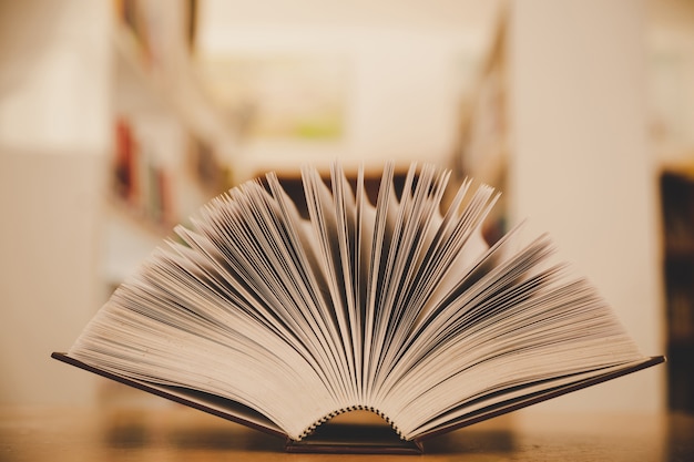 Geöffnetes Buch auf dem Schreibtisch und der Insel von Bücherregalen im Schulstudienklassenzimmerhintergrund