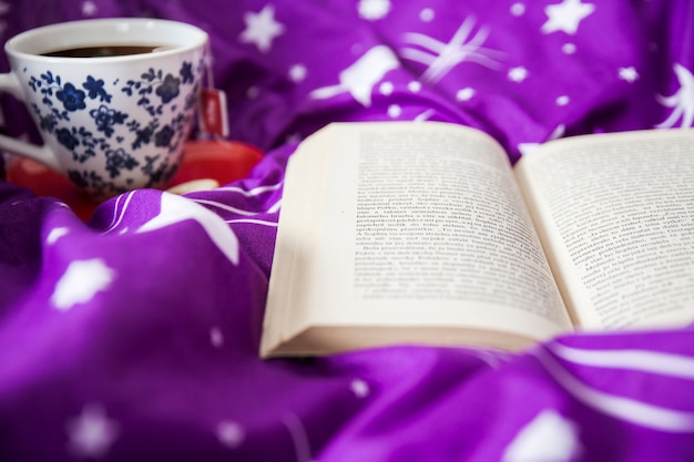 Kostenloses Foto geöffnetes buch nahe cup auf decke