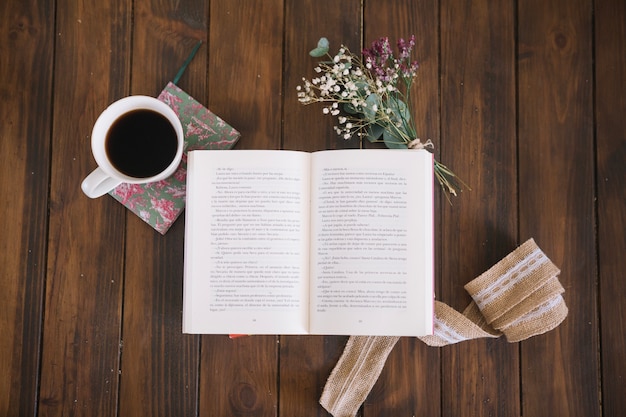 Geöffnetes Buch nahe Kaffee und Blumen