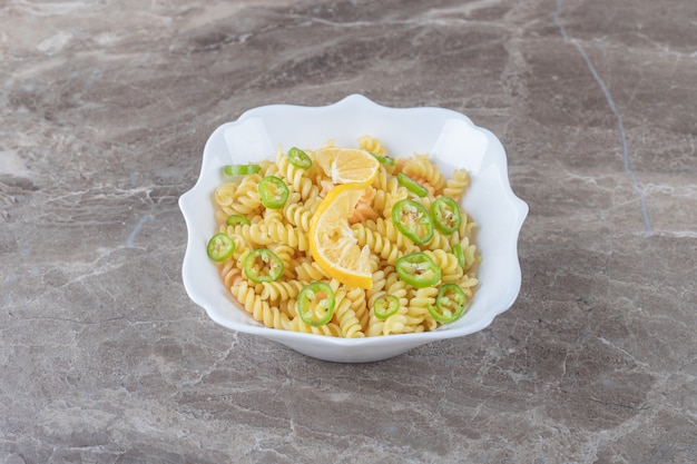 Gepfefferte Fusilli-Nudeln mit Zitronenscheibe auf Holzplatte, auf der Marmoroberfläche.