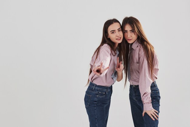 Gerade schauen und Gesten zeigen. Zwei Schwestern Zwillinge stehen und posieren