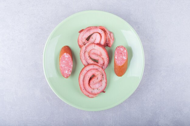 Geräucherte Fleischbrötchen und Würste auf grüner Platte.