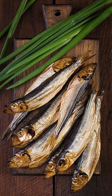 Geräucherte Sprotte und Frühlingszwiebel auf einem Schneidebrett. Geräucherter Fisch. Ansicht von oben