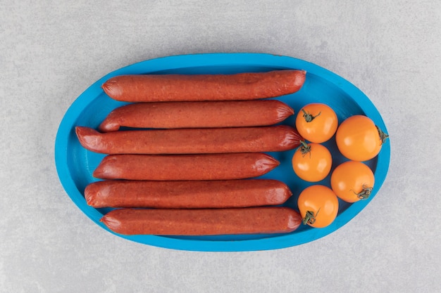 Geräucherte Würste und Tomaten auf blauem Teller.