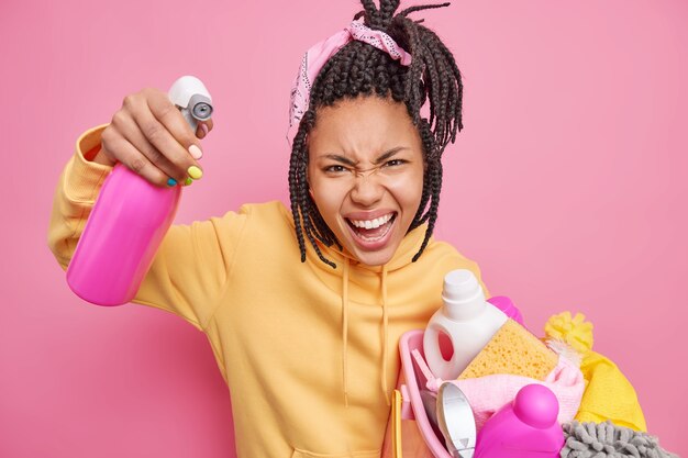 Gereiztes Hausmädchen schreit verärgert drückt negative Emotionen aus hält Becken voller Wäsche und Waschmittelflasche