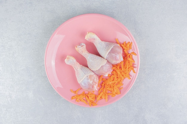 Geriebene Karotten und Hühnerschenkel auf dem Teller, auf der Marmoroberfläche