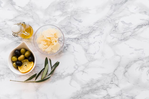 Geriebener Käse mit Oliven- und Zitronenscheibenschüssel und Ölflasche auf weißem Hintergrund