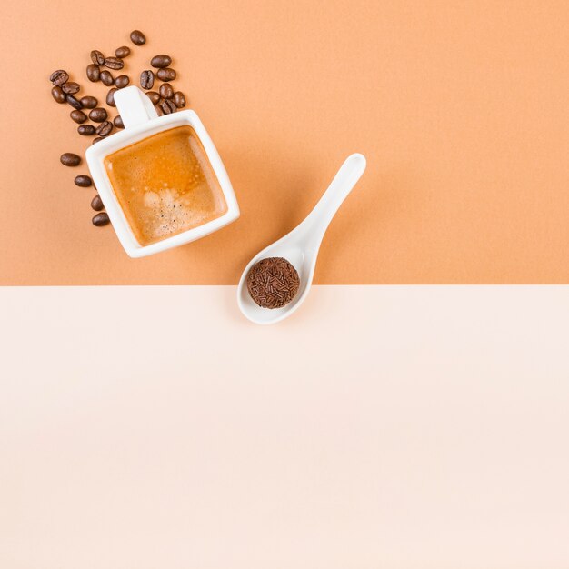 Geröstete Kaffeebohnen; Kaffeetasse und Schokoladenball im Löffel auf beige Doppelhintergrund