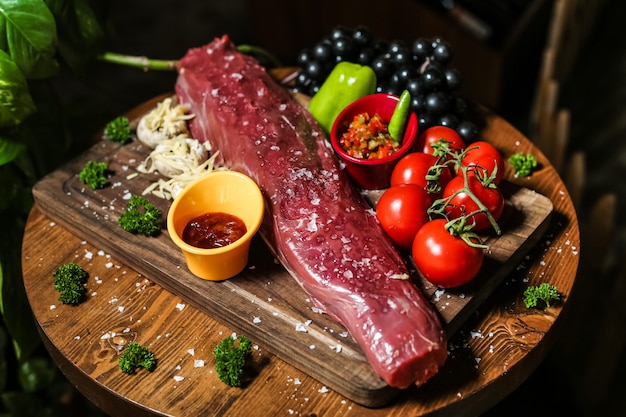 Kostenloses Foto gesalzenes rohes fleisch auf dem holzbrett mit gemüsepilzen paprika-tomatensauce seitenansicht