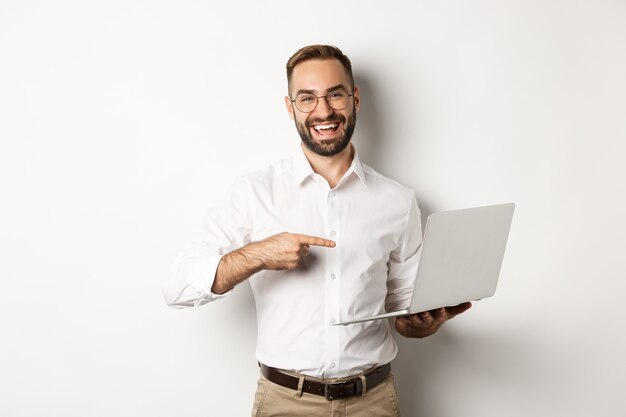 Geschäft. Hübscher Manager in der Brille, die am Laptop arbeitet, auf Computer zeigt und erfreut lächelt, stehend