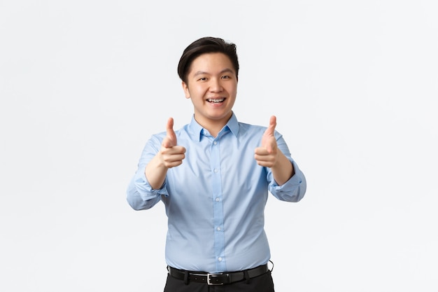 Geschäfts-, Finanz- und Menschenkonzept. Zufriedener asiatischer Geschäftsmann mit Zahnspangen mit Daumen nach oben, Büroangestellter empfiehlt Produkt oder beglückwünscht gute Arbeit, weißer Hintergrund