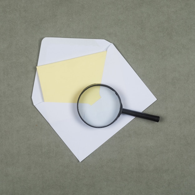 Geschäfts- und Finanzkonzept mit Brief im Umschlag, Lupe auf grauer Oberfläche flach legen.