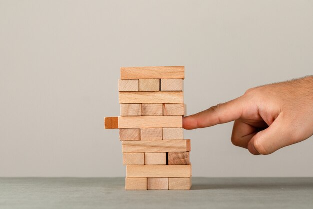 Geschäfts- und Risiko- und Managementkonzept auf grauer und weißer Wandseitenansicht. Finger schieben Holzblock Turm.