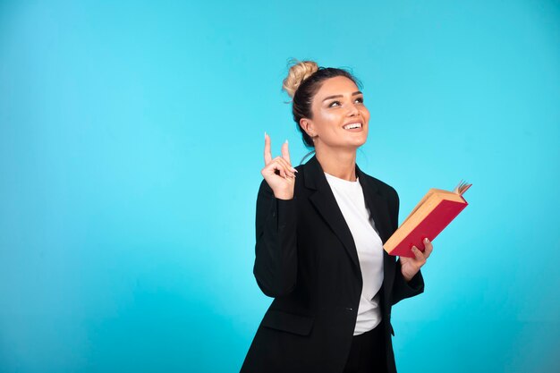 Geschäftsdame im schwarzen Blazer mit einem roten Buch, das denkt.