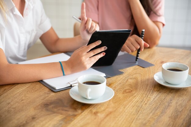 Geschäftsdamen treffen sich am Tisch, sehen sich die Präsentation auf dem Tablet an, besprechen das Projekt oder den Deal