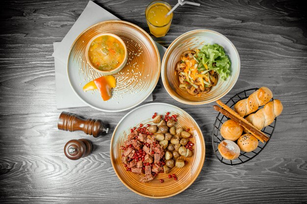 Geschäftsessen gegrilltes rotes Fleisch mit Bratkartoffeln Gemüsesuppe Pilzsalat Brot Getränk und schwarzer Pfeffer auf dem Tisch