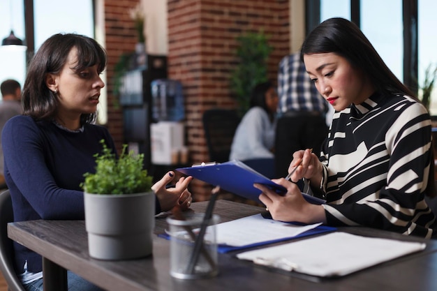 Geschäftsfrau analysiert den Lebenslauf des Bewerbers und stellt Rekrutierungsfragen während des Vorstellungsgesprächs im Büro des Startup-Unternehmens. Asiatischer Manager, der eine Frau für einen Job in der Personalabteilung rekrutiert