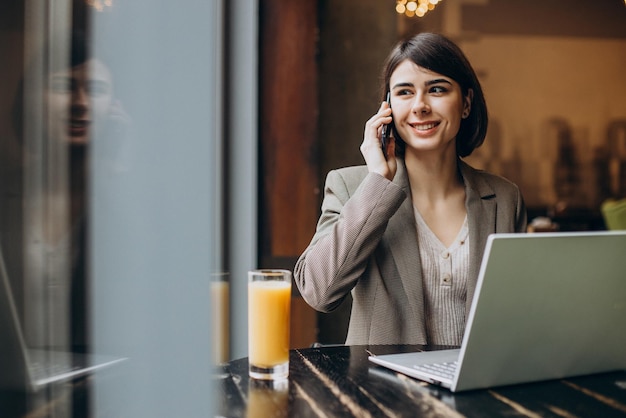 Geschäftsfrau, die am Laptop arbeitet und in einem Café am Fenster telefoniert