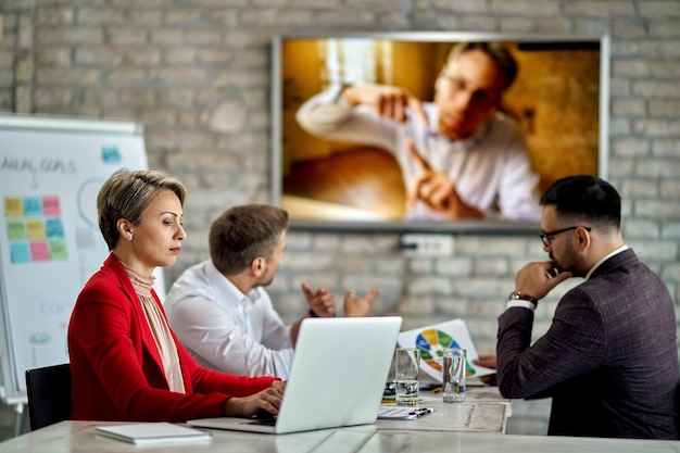 Geschäftsfrau, die an einem Computer arbeitet, während sie ein Meeting im Büro hat Einer ihrer Kollegen nimmt per Videoanruf an dem Meeting teil