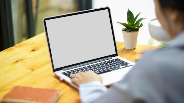 Geschäftsfrau, die an laptop-computer an ihrem schreibtisch, leeres weißes bildschirmmodell des laptops für die montage ihrer grafik arbeitet.