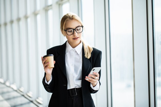 Geschäftsfrau, die eine Kaffeepause macht und Smartphone im Büro benutzt