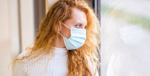 Geschäftsfrau, die eine Maske trägt und aus dem Fenster schaut