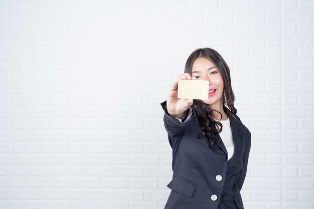 Geschäftsfrau, die eine unterschiedliche Geldautomatenkarte, weiße Backsteinmauer hält Machte Gesten mit Gebärdensprache.