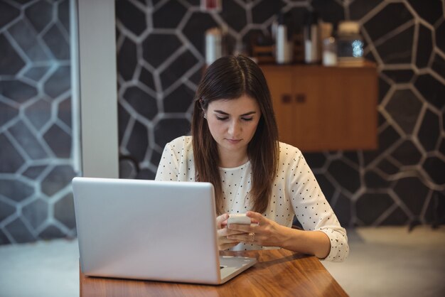 Geschäftsfrau, die Handy mit Laptop auf Tisch verwendet