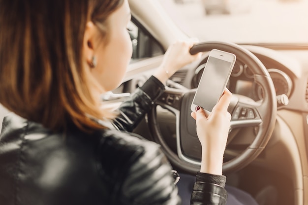 Geschäftsfrau, die im Auto sitzt und ihren Smartphone verwendet.