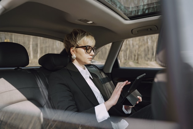 Geschäftsfrau, die in einem Auto sitzt und eine Tablette benutzt