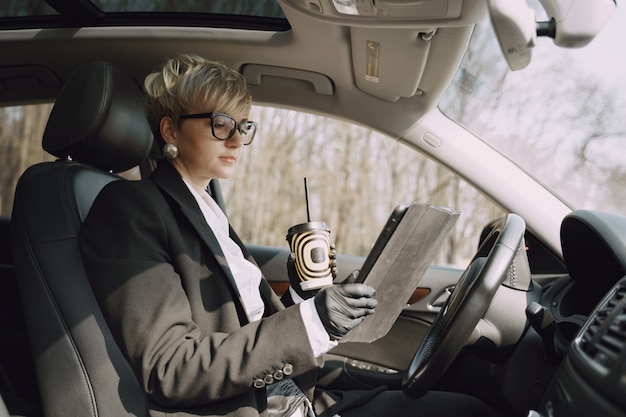 Geschäftsfrau, die in einem Auto sitzt und einen Kaffee trinkt