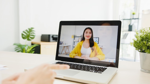 Geschäftsfrau, die Laptop verwendet, spricht mit Kollegen über den Plan in Videoanrufen, während sie von zu Hause aus im Wohnzimmer arbeitet