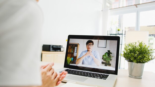 Geschäftsfrau, die Laptop verwendet, spricht mit Kollegen über den Plan in Videoanrufen, während sie von zu Hause aus im Wohnzimmer arbeitet