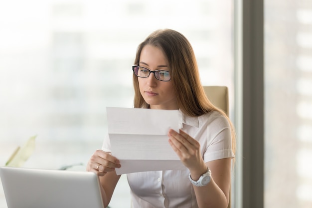 Geschäftsfrau, die offizielles Dokument am Arbeitsplatz liest