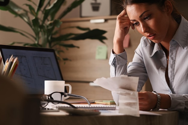 Geschäftsfrau, die sich Sorgen über Finanzschulden macht und Rechnungen analysiert, während sie im Büro arbeitet