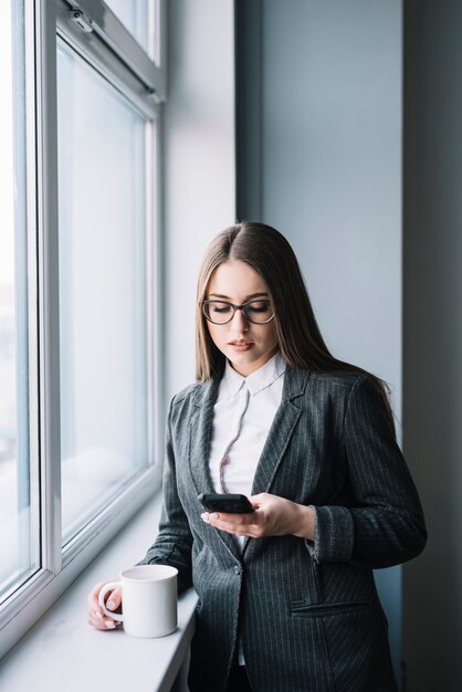 Geschäftsfrau, die Smartphone am Fenster verwendet