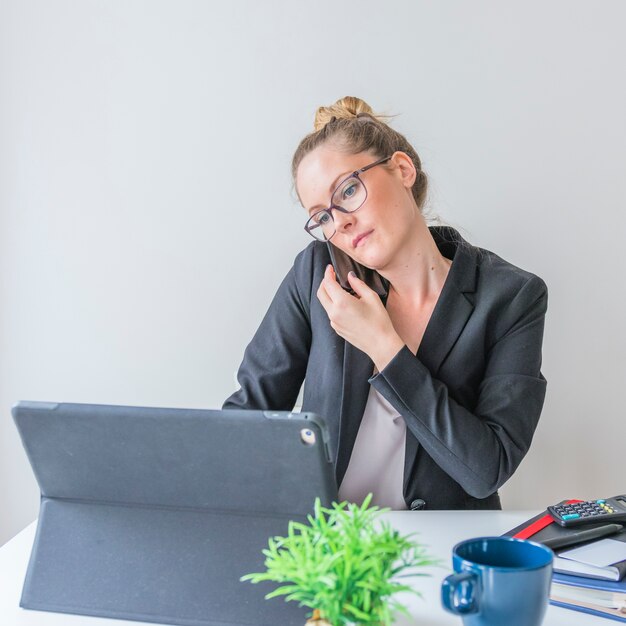 Geschäftsfrau, die Smartphone beim Arbeiten an Laptop verwendet