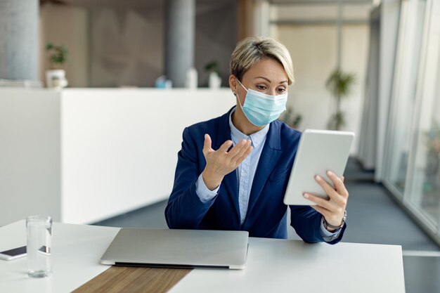 Geschäftsfrau, die während der Coronavirus-Pandemie im Büro einen Videoanruf über das Touchpad tätigt