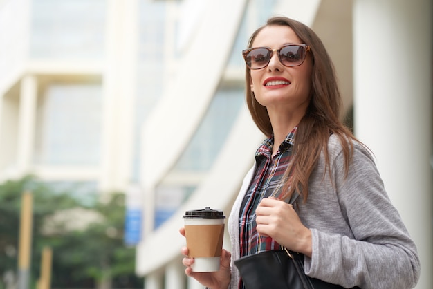 Geschäftsfrau, die weg vorangeht, um mit Mitnehmerkaffee morgens zu arbeiten