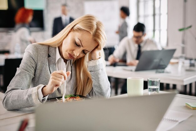 Geschäftsfrau fühlt sich während ihrer Diät deprimiert, während sie in der Mittagspause im Büro Gemüsesalat isst