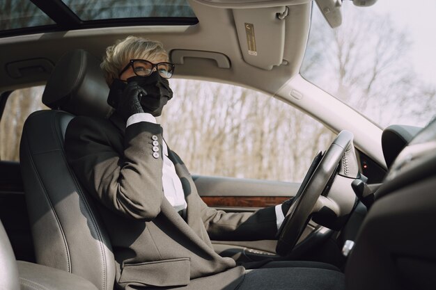 Geschäftsfrau in einer schwarzen Maske, die in einem Auto sitzt
