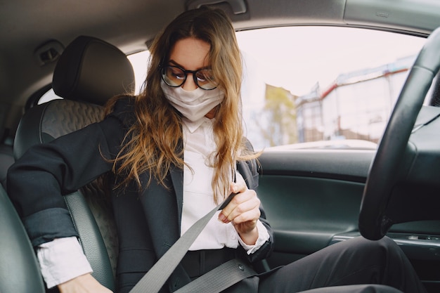 Geschäftsfrau in einer schwarzen Maske, die in einem Auto sitzt